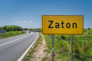 Large yellow, Zaton city welcome sign with cars on a road and green field on roadside, Croatia