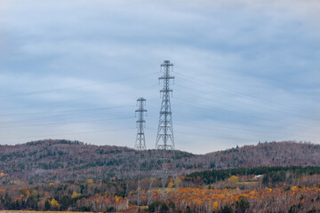 A metal electric utility pole with electrical wires, transmission lines, conductors and distribution wires for high voltage electricity. The pole have a blue sky in the background with white clouds.