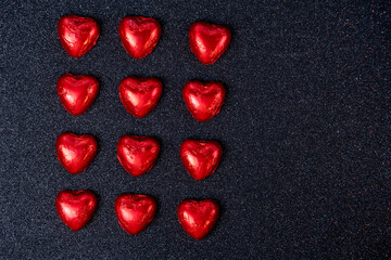heart shaped chocolates in red foil on black background with sparkles