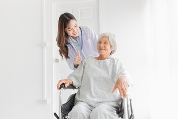 Fototapeta premium close up patient, Asian doctor drive a wheelchair and show thumb up sign with hand, doctor and old female talk about symptoms and treatment plan, rehabilitation activity, elderly healthcare promotion