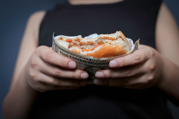 Niño sosteniendo co sus manos una hamburguesa cubierta con una billete de dólar.