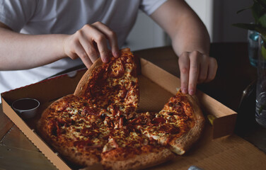 Young man eating pizza from cardboard box at home that was taken out or delivered home