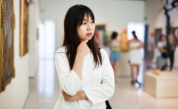 Portrait of thoughtful chinese young woman near picture collection in the museum