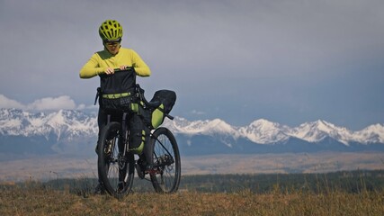 Fototapeta premium The woman travel on mixed terrain cycle touring with bikepacking. The traveler journey with bicycle bags. Sport tourism bikepacking, bike, sportswear in green black colors. Mountain snow capped.