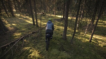Fototapeta premium The woman travel on mixed terrain cycle touring with bike bikepacking outdoor. The traveler journey with bicycle bags. Stylish bikepacking, bike, sportswear in green black colors. Magic forest park.