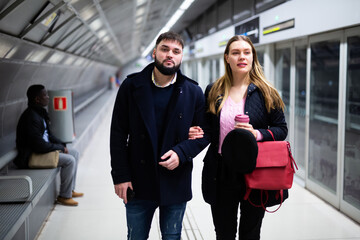 Portrait of couple of young people waiting for subway train, walking at station
