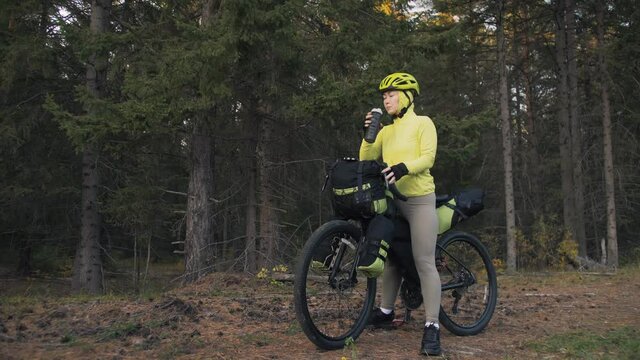 The woman travel on mixed terrain cycle touring with bike bikepacking outdoor. The traveler journey with bicycle bags. Stylish bikepacking, bike, sportswear in green black colors. Magic forest park.