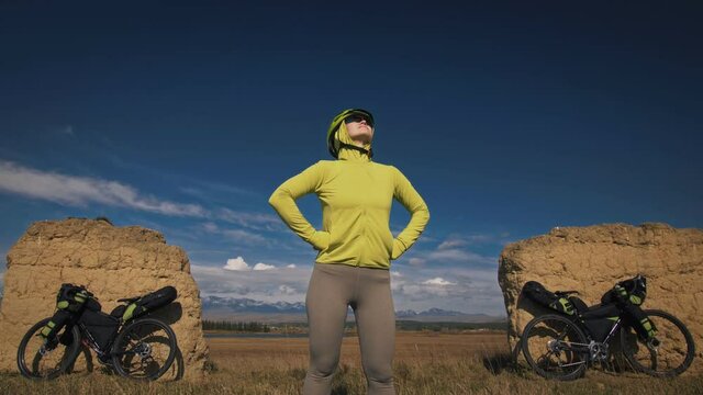 The man and woman travel on mixed terrain cycle bike touring with bikepacking. The two people journey with bicycle bags. Sport sportswear in green black colors. Mountain snow capped, stone arch.