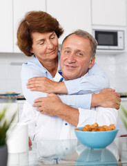 Portrait of mature family couple hugging and sitting at kitchen table while drinking tea