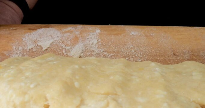 Aged female hands uses a rolling pin to stretch the dough on table. Mother preparing dough to baking cake and cookie in kitchen at home. Pensioner enjoying her new hobby. Closeup macro view.