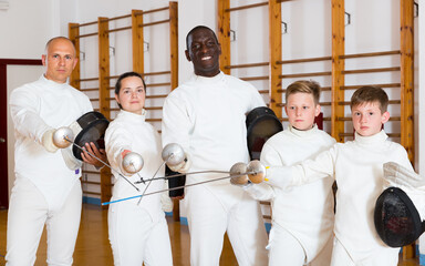 Portrait of happy athletes fencers with rapiers standing in gym.