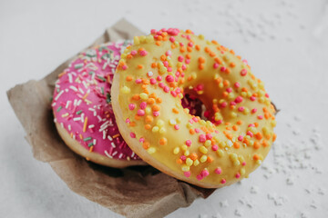 two tasty pink and yellow home made appetizing glazed donuts on kraft paper for delivery, vertical food content, selective focus