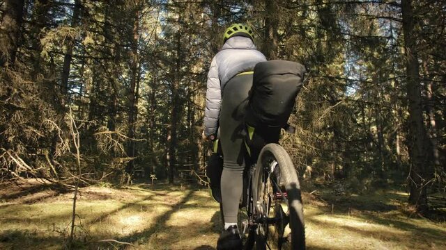 The woman travel on mixed terrain cycle touring with bike bikepacking outdoor. The traveler journey with bicycle bags. Stylish bikepacking, bike, sportswear in green black colors. Magic forest park.