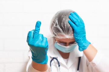 Tired exhausted desperate female doctor holding her head and showing fuck in protective medical gloves. Fighting coronavirus. Coronavirus concept. 