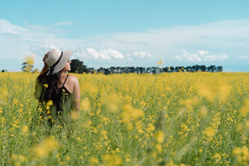 Brunette woman wearing hat on a yellow flower field during summer days