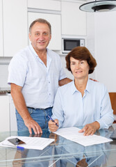Obraz premium Mature family couple sitting at kitchen and woman signing documents together