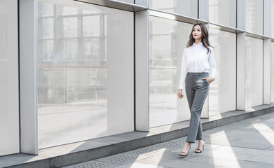 Asian business woman walking beside the outdoor glass curtain wall