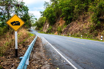 Sign on the road. Road sign with yellow background and black illustration warning truck that uphill steep slope ahead on a curvy road.
