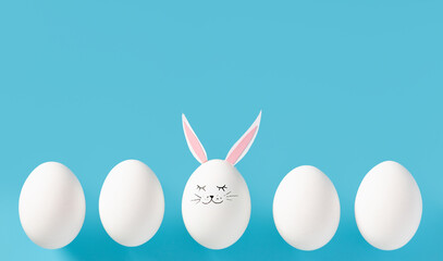 Easter eggs with bunny ears and face on blue background with copy space. Special, stands out from others. Individuality. Flat lay or top view. Minimal concept. Conceptual creative photo approaching