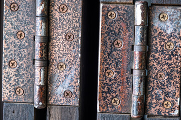 Close-up of two rusty metal door hinges on folding wooden doors.