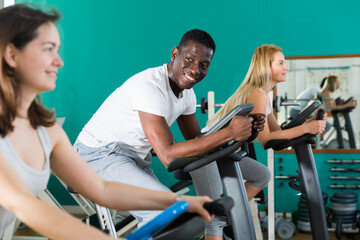 Fototapeta premium Group of three training on stationary bikes at sport club
