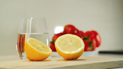 Cut lemon in half on wooden cutting board. Tomatoes and a glass of water in the background.