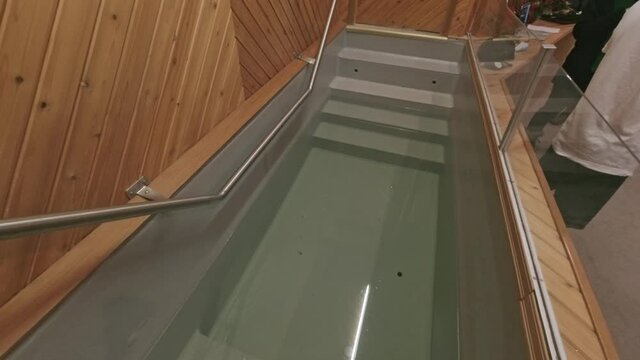 people gather at baptismal pool with steps into it during a sermony for a spiritual renewing with family and friends for a young adult with a seperation of plexiglass and railing to help participants