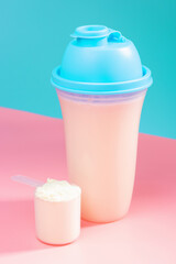 Shaker and scoop with protein on a pink and blue background.