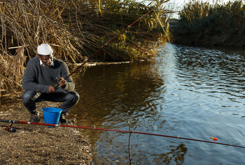 Obraz premium Portrait of cheerful afro fisherman sitting on wooden stool and fishing