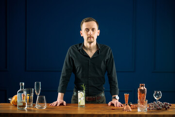 Man bartender standing behind the desk with gin tonic cocktail and tools