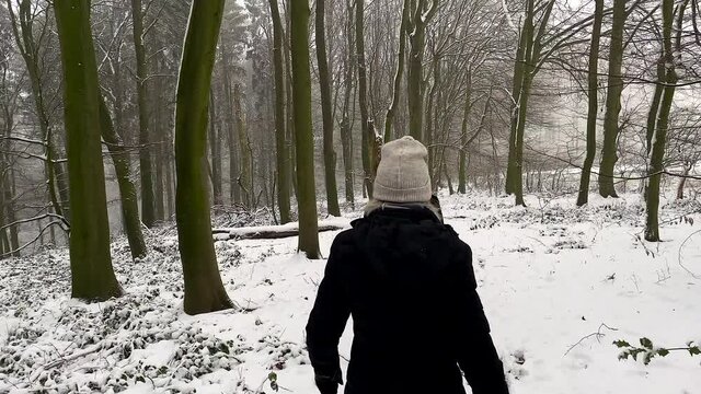 Slowmotion back view of family walking together in white winter forest during christmas time. Beautiful white covered snow landscape outdoors during cold and freezing day.