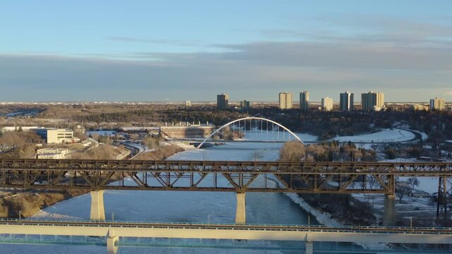 Winter Aerial fly over transit rail modern bridge next to the vintage historic low level bridge built histroically in 1910 and again in 1913 of steel held by concrete over North Saskatchewan River 1-5