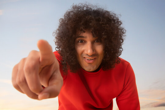 A YOUNG MAN WITH CURLY HAIR HAPPILY POINTING FINGER TOWARDS CAMERA	