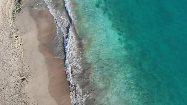 Top view of a tropical beach in the summer. Blue turquoise sea water washing on beach shores. Aerial view of a tropical beach with waves foaming in the sand. Sunny beach water wave during the summer