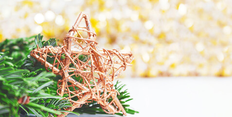 Banner with golden wooden star and natural fir tree branch in christmas composition. Christmas winter background with abstract shiny golden bokeh background. Selective focus. Copy space.
