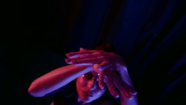 Portrait of a beautiful woman with an unusual pattern and with rhinestones on her face posing in front of the camera in a dark studio, making movements with her hands.