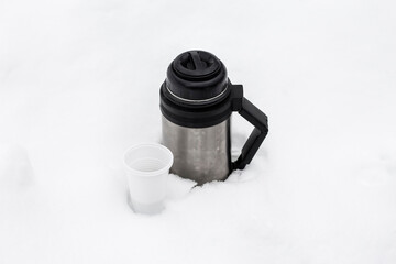 thermos with hot tea and a disposable glass in winter in a snowdrift in nature