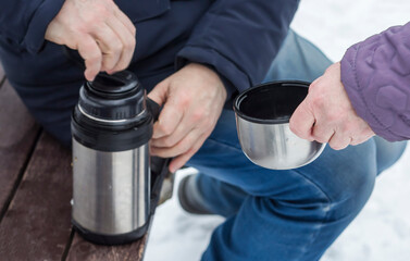 a woman is waiting for tea holding out a cup to a thermos of hot tea