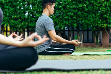 Young Asian couple man and woman practicing yoga in the garden. Summer morning