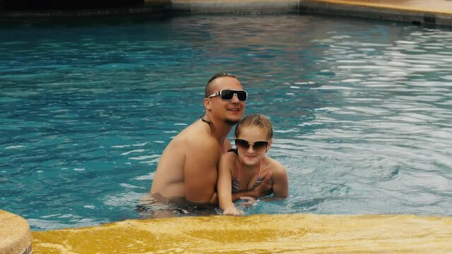 The father with little daughter have fun in the pool. Dad plays with the child. The family enjoy summer vacation in a swimming pool jumping, spinning, splash water. Slow motion.