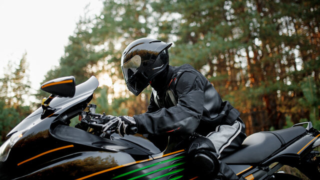 Motorcyclist in a helmet and leather protective gear close-up looks straight, sitting on a fast sports motorcycle