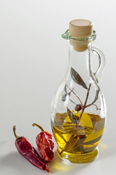 Olive oil and olive sprig in a glass jug on a white background. Hot red pepper pods nearby.  Close-up. Vertical position.