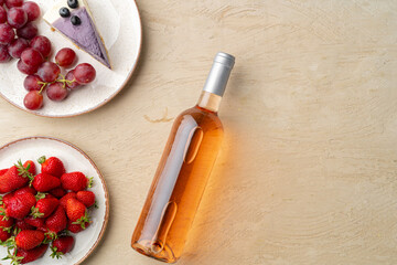 Bottle of pink wine, fruits and piece of cheesecake on gray background flat lay