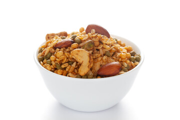 'Shahi Mixture' in a white ceramic bowl, made with peanut, cashew, corn flakes, almonds, etc. Pile of Indian spicy snacks (Namkeen). Side view, against the white background