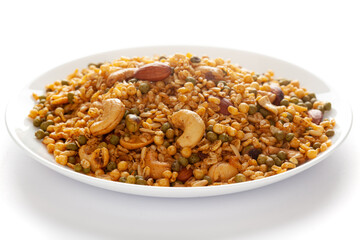 'Shahi Mixture' in a white ceramic plate, made with peanut, cashew, corn flakes, almonds, etc. Pile of Indian spicy snacks (Namkeen). Side view, against the white background