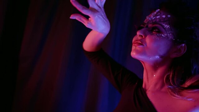 Portrait of a beautiful woman with an unusual pattern and with rhinestones on her face dancing in front of the camera in the studio against the background of curtains.