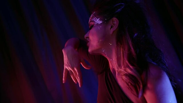 A beautiful woman with unusual makeup, a pattern and with rhinestones on her face dances in front of the camera in the studio against the background of curtains. Makes dance moves.