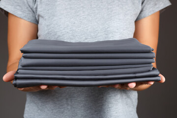 A woman holds a stack of clean folded gray bed sheets.