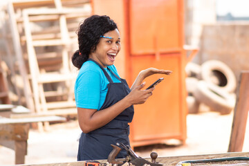 pretty female african carpenter feeling excited and happy while holding her phone