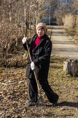 An elderly woman collects fallen leaves with a broom